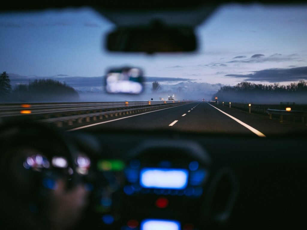 View through a windshield onto a misty highway at dusk, with a glowing dashboard